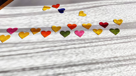 Multicolored hearts made of rough velvet paper on white surface with stripes of shadow and light...