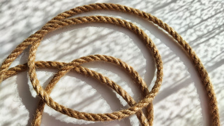 Jute twisted rope lying on a white surface with shadows from the sun. Abstract background, texture,...