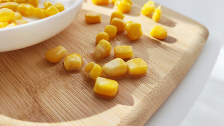 Lot of pieces of canned yellow corn on plate which is on wooden bamboo cutting board on white background. Concept of cooking and delicious food healthyの写真素材