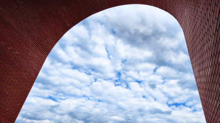View of textured sky with white and blue clouds through a brick or stone arch. Abstract background,...