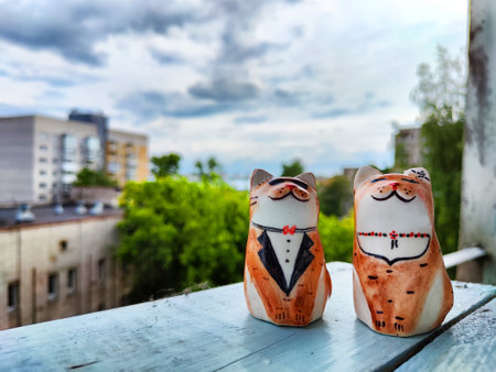 Porcelain figurines of couple of cats in men's and women's costumes on high balcony against the backdrop of city houses and trees. The concept of love, comfort, convenience, and careの写真素材