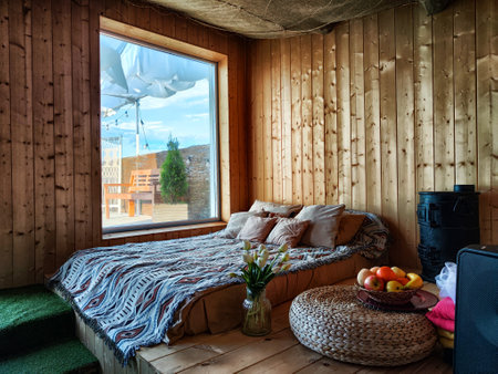 Bright room with a large window and bed. Interior of a bedroom or living room with a wide bed and summer outside the windowの写真素材