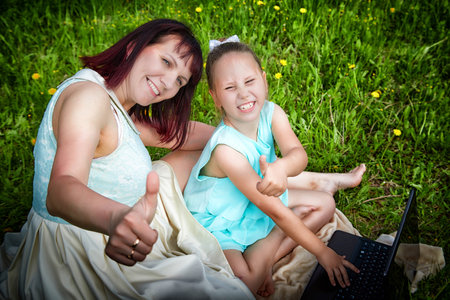 Kirov, Russia - May 18, 2023: Mom and Daughter with laptop resting on a green lawn or a field in park in nature. Fmily with a mother and girl on the Internet, chatting, communicating with relativesのeditorial素材