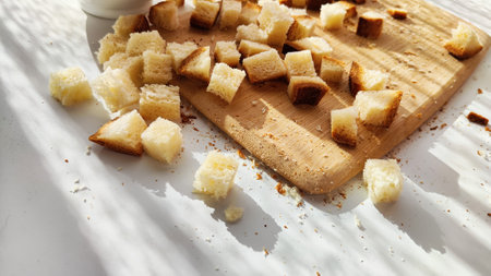 Homemade slices of diced dry white rye bread on cutting board and white plate. Crackers for food,...