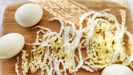 Chopped Peking cabbage and peeled eggs on cutting board as background. Cooking a healthy eco-friendly salad from natural products. Copy space and place for textの写真素材
