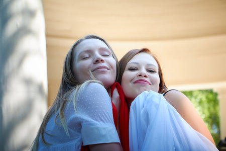 Kirov, Russia - August 10, 2021: Two girls, young women, sisters are walking in the park and waving a white and red cloth on a sunny spring or summer day. Models pose for a photo shootのeditorial素材