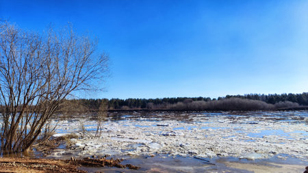 Spring landscape with water and ice on river and blue sky in background in sunny day. Ice drift and flood on river with sunの写真素材