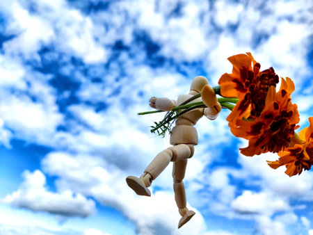 Wooden toy man with flowers and sky full white clouds on backgroudn. Concept of holiday, bouquet, Valentine's Day, proposal, engagement, declaration of love, Mother's Day. Caring, loving, romanticの写真素材