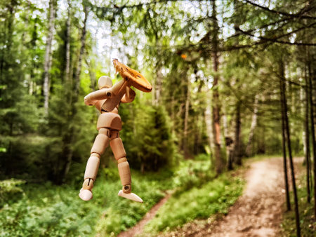 Wooden toy mannequin in a summer or autumn forest with a mushroom. The concept of mushroom picking, nature walk, autumn abundanceの写真素材