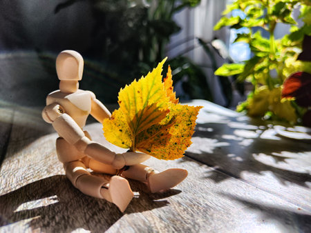 Small wooden figurine with a bouquet of autumn yellow birch leaves, bathed in sunlight, surrounded...
