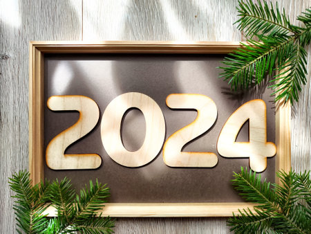 Wooden figures and numbers of the new year 2024 with frame and fir branches of Christmas tree. celebration. Abstract background, pattern, frame, place for text, copy spaceの写真素材