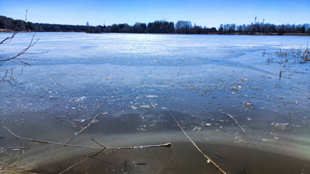 Landscape with a lake covered with ice before the start of melting and ice drift on spring day with the sun. Blue ice and water under sunlight in early spring or autumnの写真素材