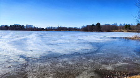Landscape with a lake covered with ice before the start of melting and ice drift on spring day with the sun. Blue ice and water under sunlight in early spring or autumnの写真素材