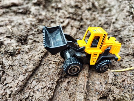 Small yellow toy tractor is working outside. The concept of the effectiveness of technology in...