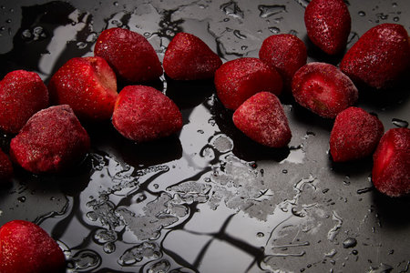 Red Frozen strawberries on a wet black background. Pattern, texture, frame, place for text, copy spaceの写真素材