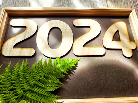 Wooden figures and numbers of new year 2024 with frame and green fern leaves. Celebration. Abstract...