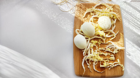 Chopped Peking cabbage and peeled eggs on cutting board as background. Cooking a healthy eco-friendly salad from natural products. Copy space and place for textの写真素材