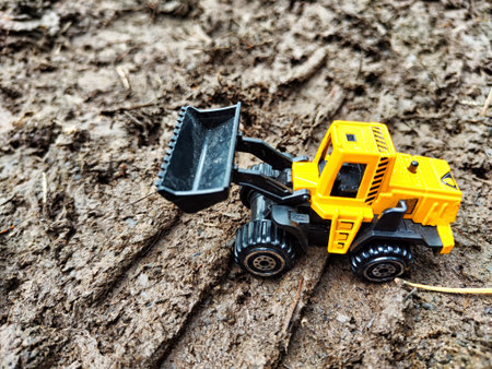 Small yellow toy tractor is working outside. The concept of the effectiveness of technology in...