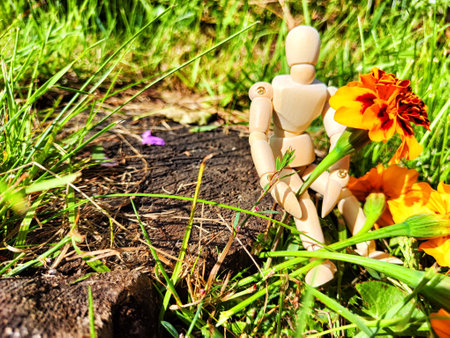 Wooden toy man with flowers against background grass in nature. Concept of holiday, gift bouquet, Valentine's Day, proposal, engagement, declaration of love, Mother's Day. Caring, loving and romanticの写真素材