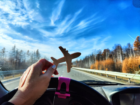 Small wooden toy airplane in the female driver's hand in car on the background of the road and...