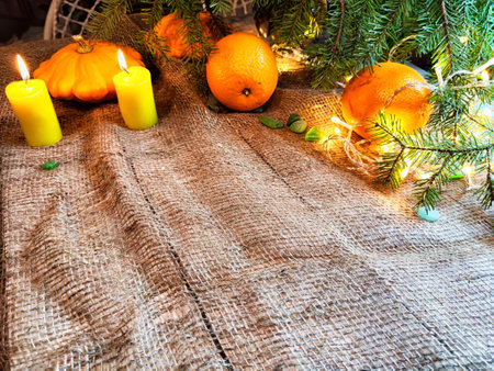 Festive decoration with bouquet and branches of spruce, bright glowing garlands and candles, burlap, oranges. Background for Christmas, New Year. Abstract texture, frame, place for text, copy spaceの写真素材