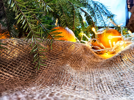 Festive decoration with bouquet and branches of spruce, bright glowing garland, orange, burlap on wooden background. Decor for Christmas, New Year. Abstract texture, frame, place for text, copy spaceの写真素材