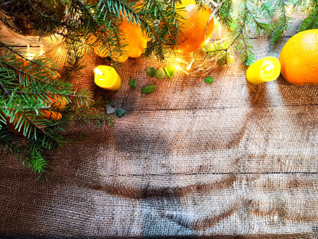 Festive decoration with bouquet and branches of spruce, bright glowing garlands and candles, burlap, oranges. Background for Christmas, New Year. Abstract texture, frame, place for text, copy spaceの写真素材