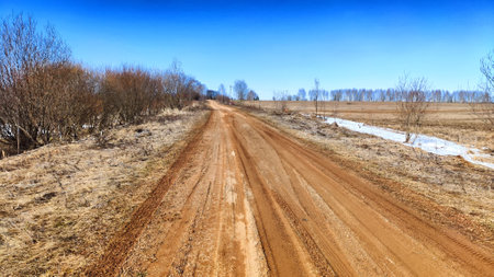 Dry dirt clay rural road in a field, stretching to the horizon in early spring. Rustic landscapeの写真素材