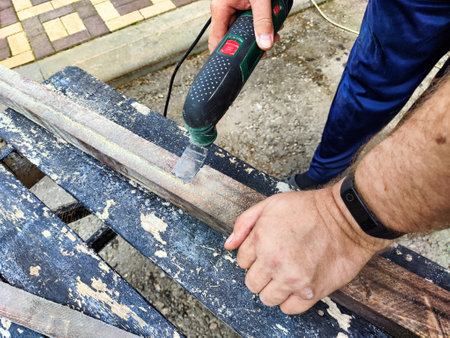Hands of a master carpenter with an electric jigsaw in his hands cutting off piece of wood. Male...