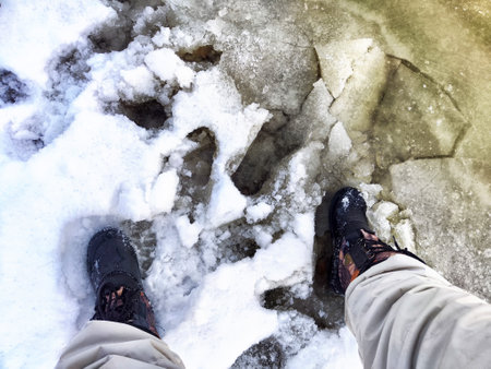 Feet of Hunter or fisherman in big warm boots on winter day on snow. top view. Fisherman on the ice of a river, lake, reservoir on spring day with melting ice. Dangerous fishing in autumnの写真素材