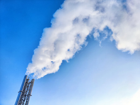 Air pollution by smoke coming out of two factory chimneys. White clouds of smoke against a blue sky backgroundの写真素材