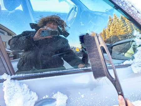 Winter Morning Car Snow Clearing. Woman person brushing snow off car on frosty winter morning and...
