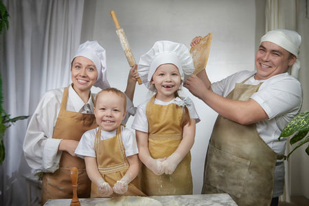 Cute oriental family with mother, father, daughter, son cooking in the kitchen on Ramadan, Kurban-Bairam, Eid al-Adha. Funny fighting parents at cook photoshoot. Pancakes, pastries, Maslenitsa, Easterの写真素材
