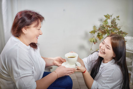 Happy Overweight family with mother and daughter drinking tea or coffee in room. Middle aged woman and teenager girl having fun, joyの写真素材