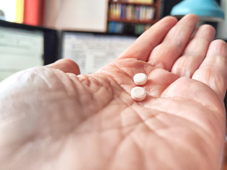 Close-up of an adult hand holding two small white pills. Close-Up of Two Pills in an Open woman Palm...