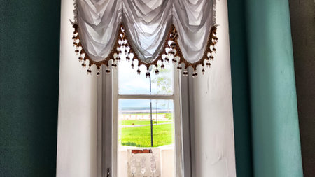 Elegant Window Drapes With Tassel Trim Overlooking a Sunny Day. White sheer curtains with decorative...