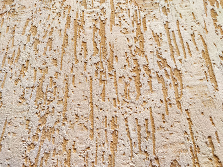 Peeling Beige Paint on Rough Wall Texture. Weathered wall with flaking paint exhibiting aging