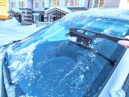 Winter Morning Car Snow Clearing. Person brushing snow off car on frosty winter morning. Difficulties in travel and trip in cold monthsの写真素材