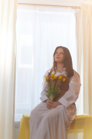 Beautiful sweet girl in nightgown in early morning with bouquet of delicate yellow tulips. Gift on International Womens Day on March 8th. Cosmetics, skin care, hair care. Perfume, natural fragranceの写真素材