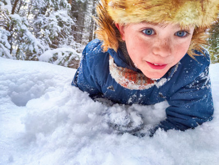 Disabled boy without an arm crawls through the snow while playing snowballs in winter in a...