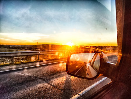 The side mirror of the car and the sun with bright rays behind it and the track on trip in natureの写真素材