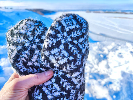 A hand with patterned woolen mittens gives thumbs up against a clear, snowy landscapeの写真素材