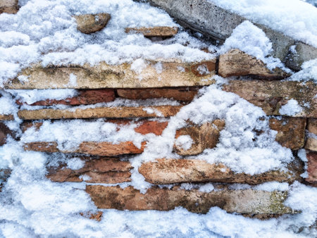 Snow rests on the textured surface of a brick wall. Background, texture, pattern, copy spaceの写真素材