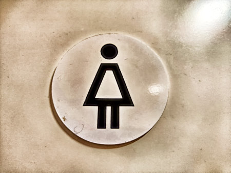 A close-up ofa white, circular sign with a black female symbol on a beige wallの写真素材