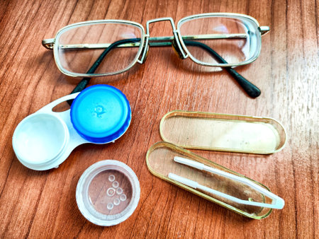 Close-up of eyeglasses, contact lens case, and tweeters on wooden surfaceの写真素材