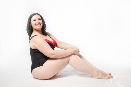 Portrait of attractive dreamy thick woman in red black swimsuit posing on white background. Body positive, photo shoot, selfie. Funny plus size modelの写真素材