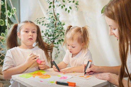 Young mother or babysitter, little daughter, sister teenager girl drawing at table in room....