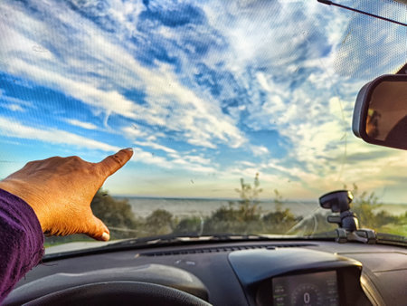 Car salon, windshield, hand on steering wheel and landscape in cloudy weather. View from driver on nature with Road. Partial focus. Blurredの写真素材