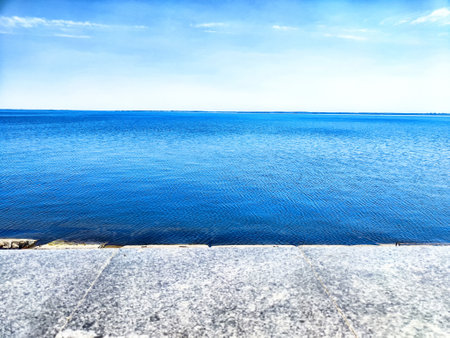 A calm blue sea, clear sky with white clouds, and rocky shorelineの写真素材