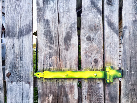 A close-up view of metal hinged painted yellow and green attached to a weathered wooden fenceの写真素材